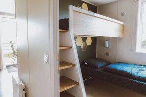 Ein kompaktes Zimmer mit Etagenbett, kleinem Schreibtisch und Stuhl. Ein Fenster sorgt für natürliches Licht.