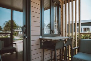 Ein Balkon mit einem Holztisch und Stühlen, großen Fenstern und Blick ins Freie.