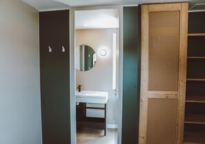 Ein Badezimmer mit einem weißen Waschbecken, einem runden Spiegel und einer Holztür mit Flechtpaneel.
