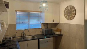 Une cuisine équipée d’un évier, d’une cuisinière, d’un four à micro-ondes et d’une horloge murale.