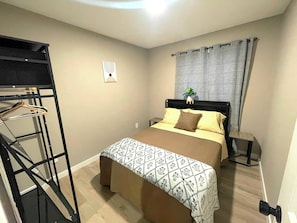 Un dormitorio con cama, mesita de noche, armario ropero y ventana con cortinas.