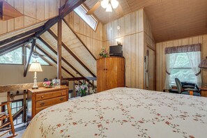Une chambre à coucher avec un grand lit, des murs en bois, un bureau avec une lampe et un téléviseur posé sur un meuble.