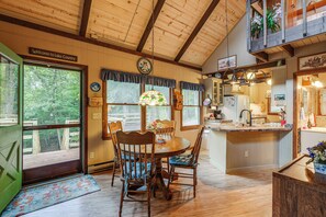 A wooden interior with a dining table, chairs, a kitchen area, and a view of the outdoors through large windows.