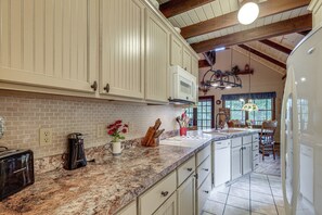 A kitchen with white cabinets, a granite countertop, a built-in microwave, and a hanging light fixture.
