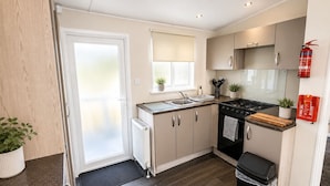 A compact kitchen with a stove, sink, and cabinets, a small window with a plant, and a fire extinguisher on the wall.