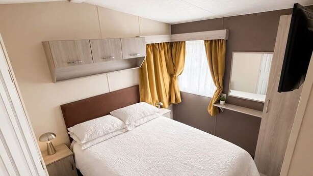 A hotel room with a bed, a nightstand, a mirror, a wardrobe, and a window with curtains.
