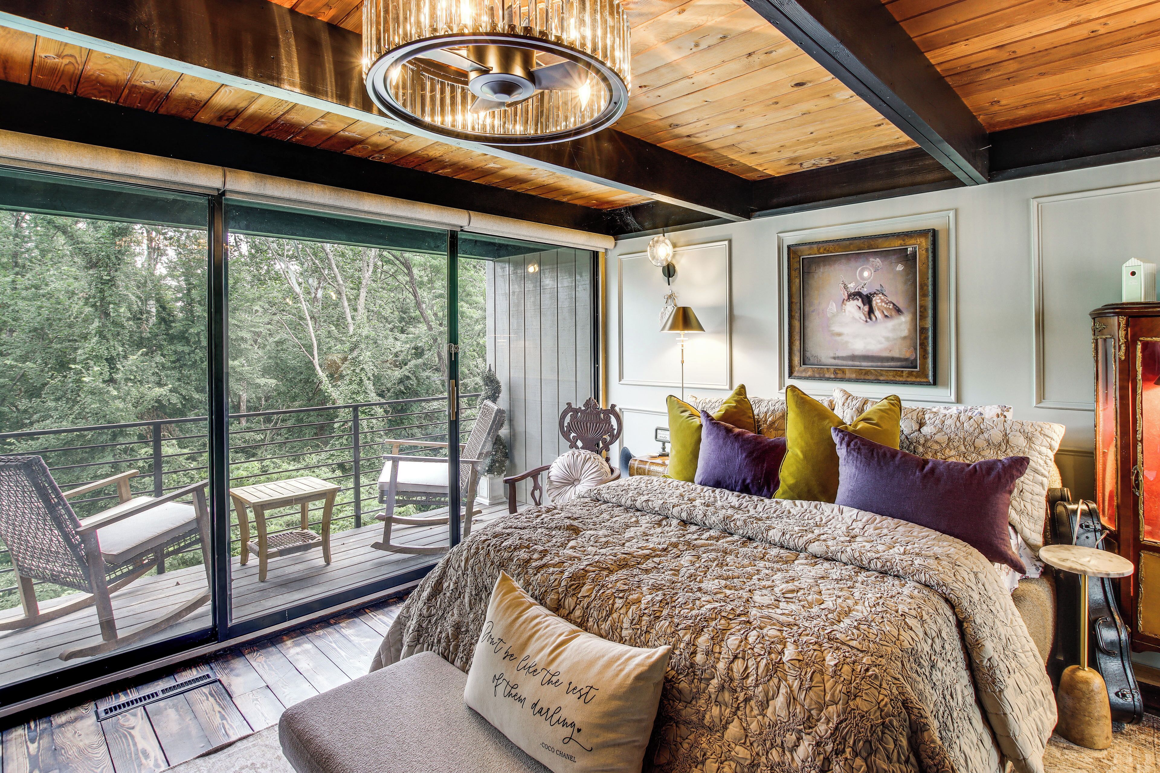 A bedroom with a large bed, a view of the outdoors, and a balcony with furniture.