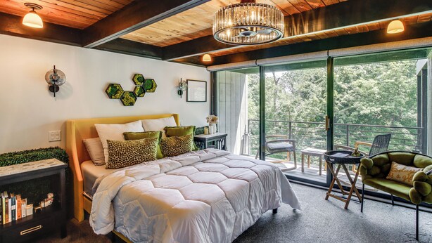 A bedroom with a large bed, a nightstand, a reading lamp, and a view of the outdoors through a sliding door. - Award-Winning Mr Mid-Modern-Century (Iowa City)