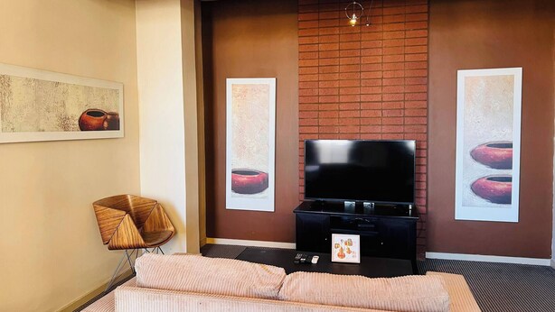 A hotel room with a large bed, a flat-screen TV, and a brick accent wall.