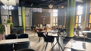 A modern restaurant interior with high tables and chairs, ambient lighting, and a view through a glass partition.