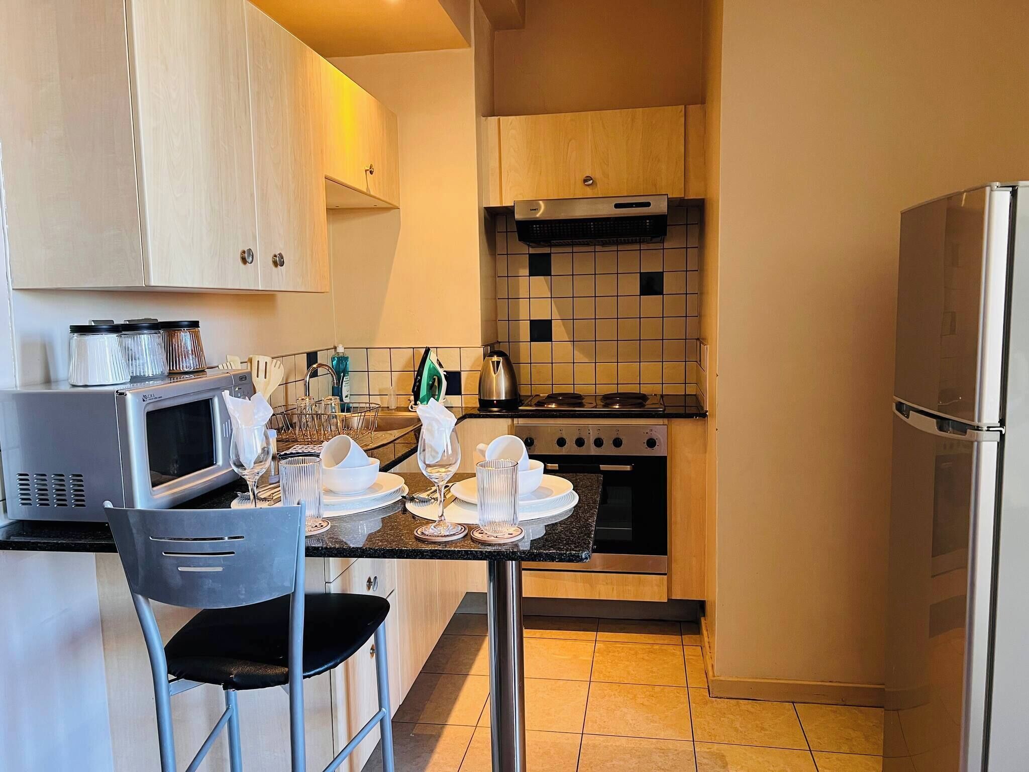 Cocina compacta con microondas, estufa y refrigerador. Cuenta con una mesa de comedor con sillas y una pequeña isla con pileta.