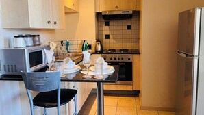 A compact kitchen with a microwave, stove, and refrigerator. There is a dining table with chairs and a small island with a sink.