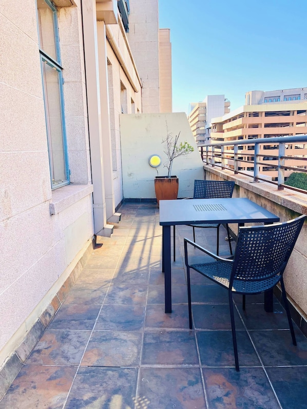 A rooftop terrace with a table and chairs, a potted plant, and a view of surrounding buildings.