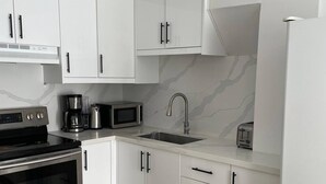 Uma cozinha moderna com armários brancos, micro-ondas embutido, cafeteira e pia.