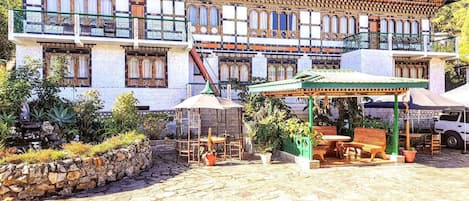 A traditional building with a balcony, outdoor seating area with tables and chairs, and a stone pathway.
