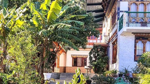 Un patio con un edificio tradicional, plantas en macetas y un banco verde.