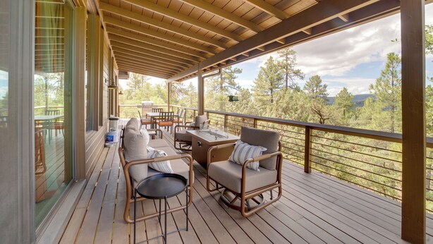 A wooden deck with outdoor furniture, including chairs and a table, overlooking a forested landscape. - Sunset Views + Scenic Trails: Spacious Pine Escape (Pine)