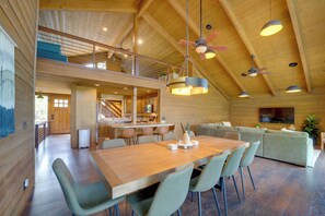 Un vaste espace de vie doté d’un plafond haut, de poutres en bois et d’une table à manger avec des chaises.