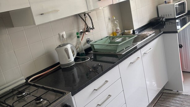 Una cocina con armarios blancos, cocina a gas, microondas y hervidor.