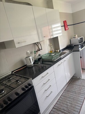 A kitchen with white cabinets, a gas stove, a microwave, and a kettle. - Charming Double Room in Shared Lisbon (Lisbon)