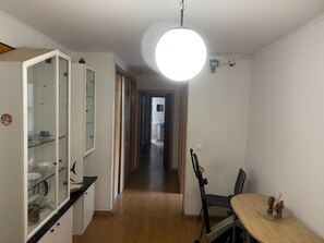 Ein schmaler Flur mit Essbereich auf der einen Seite, Küchenzeile auf der anderen und einem am Ende sichtbaren Badezimmer durch eine geöffnete Tür.