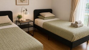Habitación de hotel con dos camas, una mesita de noche con lámpara, un cuadro enmarcado en la pared y vistas al exterior por la ventana.