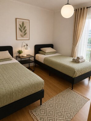 Ein Hotelzimmer mit zwei Betten, einem Nachttisch mit Lampe, einem gerahmten Bild an der Wand und Blick ins Freie durch das Fenster.