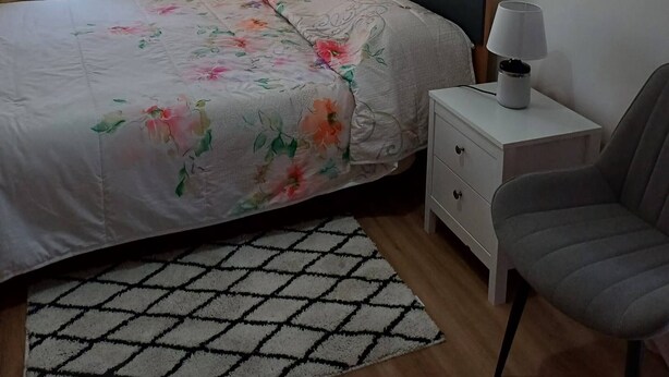 A bedroom with a bed, a nightstand, a chair, a lamp, a painting, and a window with curtains. - Quiet 3-Bedroom Apartment Povoa (Póvoa de Santa Iria)