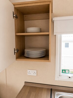 A kitchen with wooden cabinets, a window with blinds, and a power outlet.
