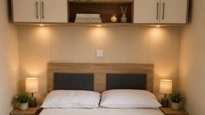 Ein ordentlich bezogenes Bett mit Kopfteil, zwei Nachttische mit Lampen und einem Regal darüber.