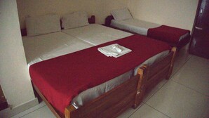 A single bed with a red bedspread, a wooden headboard, and a white pillow on the bed. - Chandrika Tourist Home (Kanayannur)