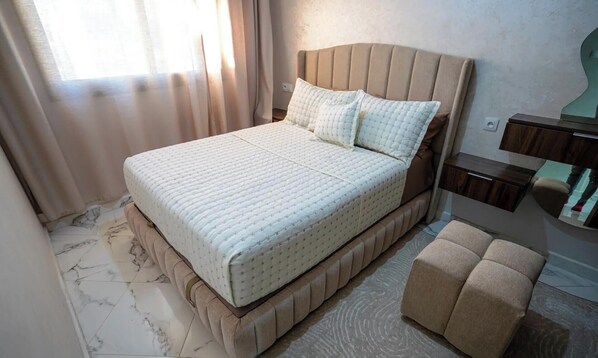 A bedroom with a bed, a bedside table, a mirror, and a window with curtains. - Charming 2-Bedroom   Apartment in Martil with City Views (Martil)