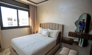 A hotel room with a bed, a window, a mirror, and a bedside table. - Charming 2-Bedroom   Apartment in Martil with City Views (Martil)