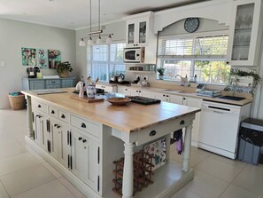 A spacious kitchen with a central island, white cabinetry, and a large window providing natural light. - Cornerhouse Family Retreat (Cape Town)