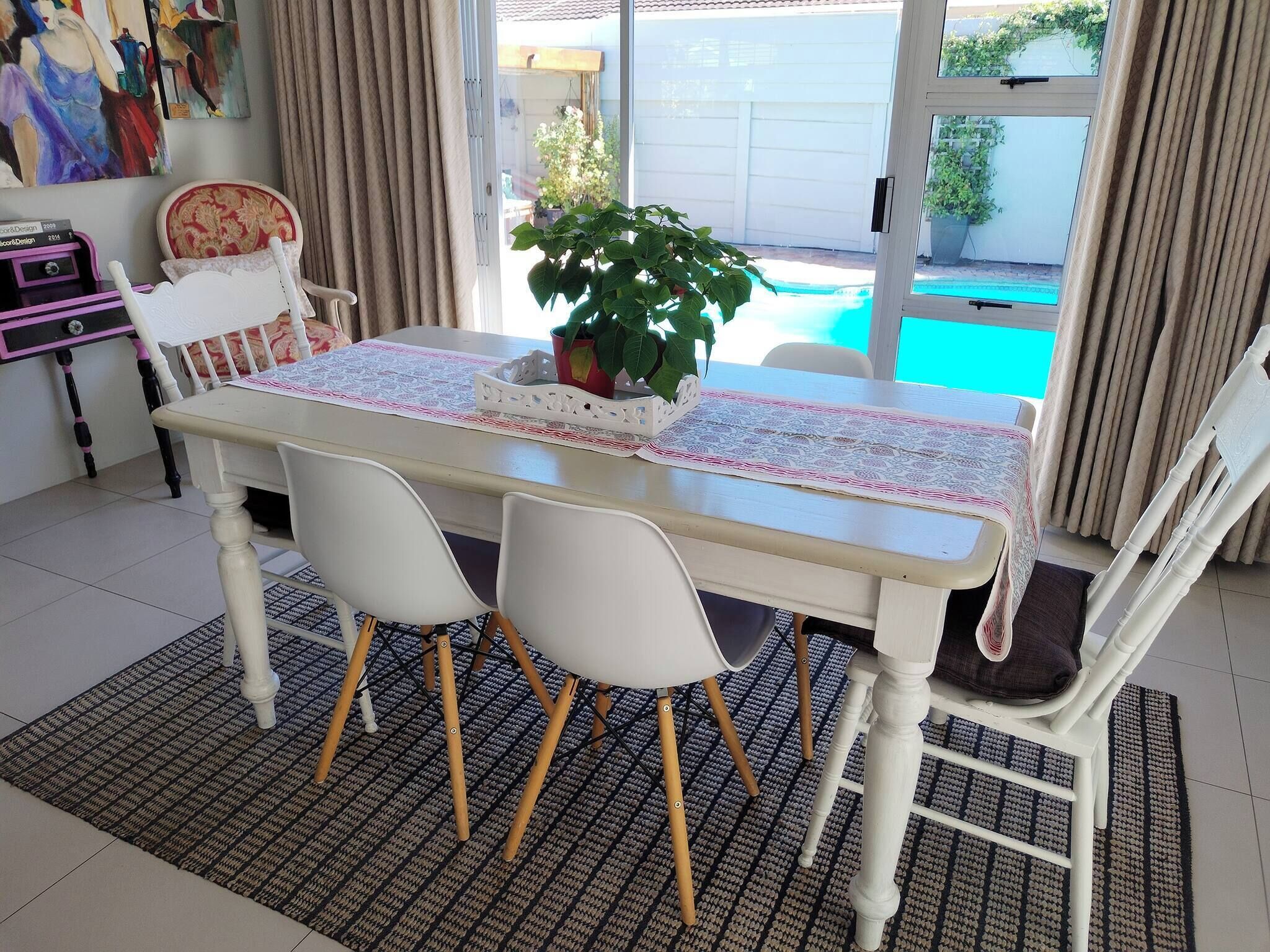 A dining area with a table, chairs, a potted plant, and a view of a swimming pool.