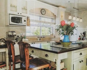 A kitchen with a central island, wooden chairs, a clock, and a window with a view. - Cornerhouse Family Retreat (Cape Town)