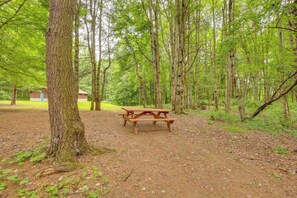 A picnic table in a forested area with trees and a small building in the background.