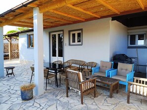 Eine überdachte Terrasse im Freien mit Steinboden, Korbmöbeln und einem Grill.