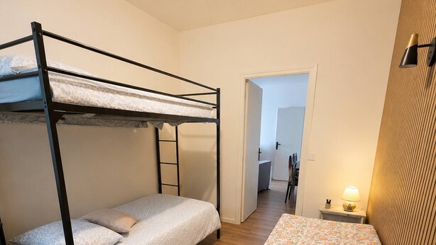 A bunk bed room with a wooden floor, a desk with a lamp, and a door leading to another room. - T3 Montluçon-gare à 15 min à pied (Montluçon)