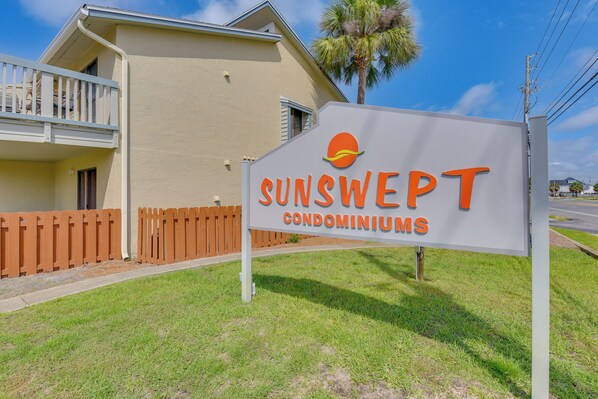 Une enseigne indiquant le complexe de copropriétés SUNSWEEP, avec une vue dégagée sur un immeuble et un palmier.