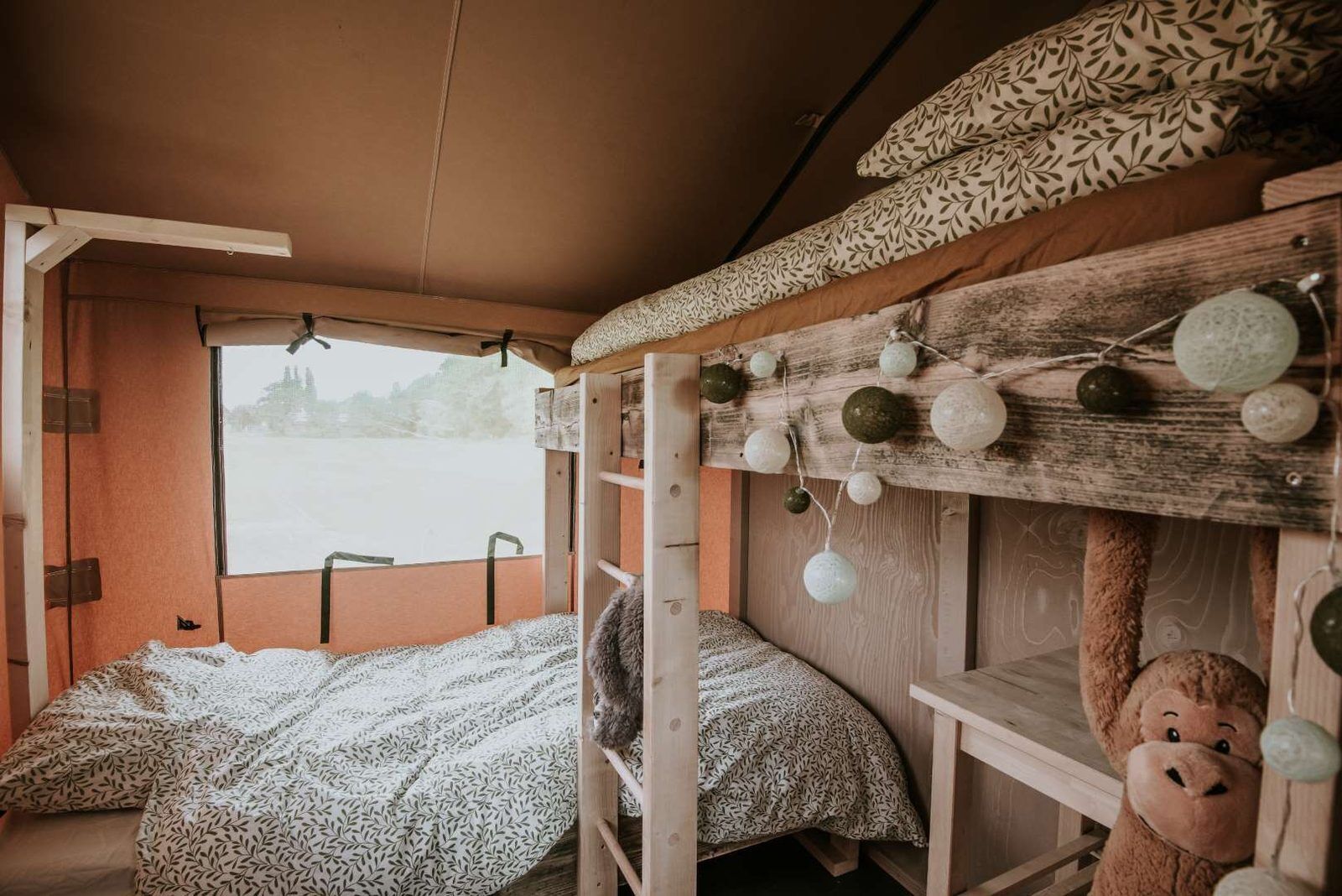 A bunk bed with patterned bedding, a window with a view, and a stuffed toy on the lower bunk.
