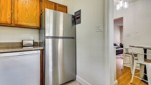 A kitchen with wooden cabinets, a stainless steel refrigerator, a dishwasher, and a dining area with a table and chairs. - Corner Unit 2 Mi to UNCG & Downtown Greensboro! (Greensboro)