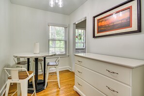 Une pièce avec un bureau blanc, deux chaises, une commode et un tableau encadré accroché au mur.