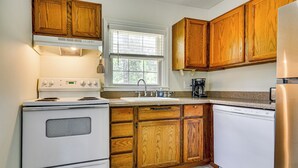 A kitchen with wooden cabinets, a white stove, a sink, and a coffee maker. - Corner Unit 2 Mi to UNCG & Downtown Greensboro! (Greensboro)