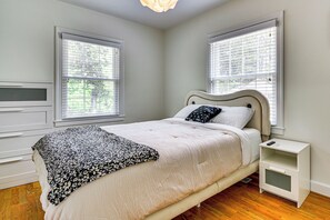 Ein Schlafzimmer mit einem Bett, zwei Fenstern, einem Nachttisch und einer Kommode.