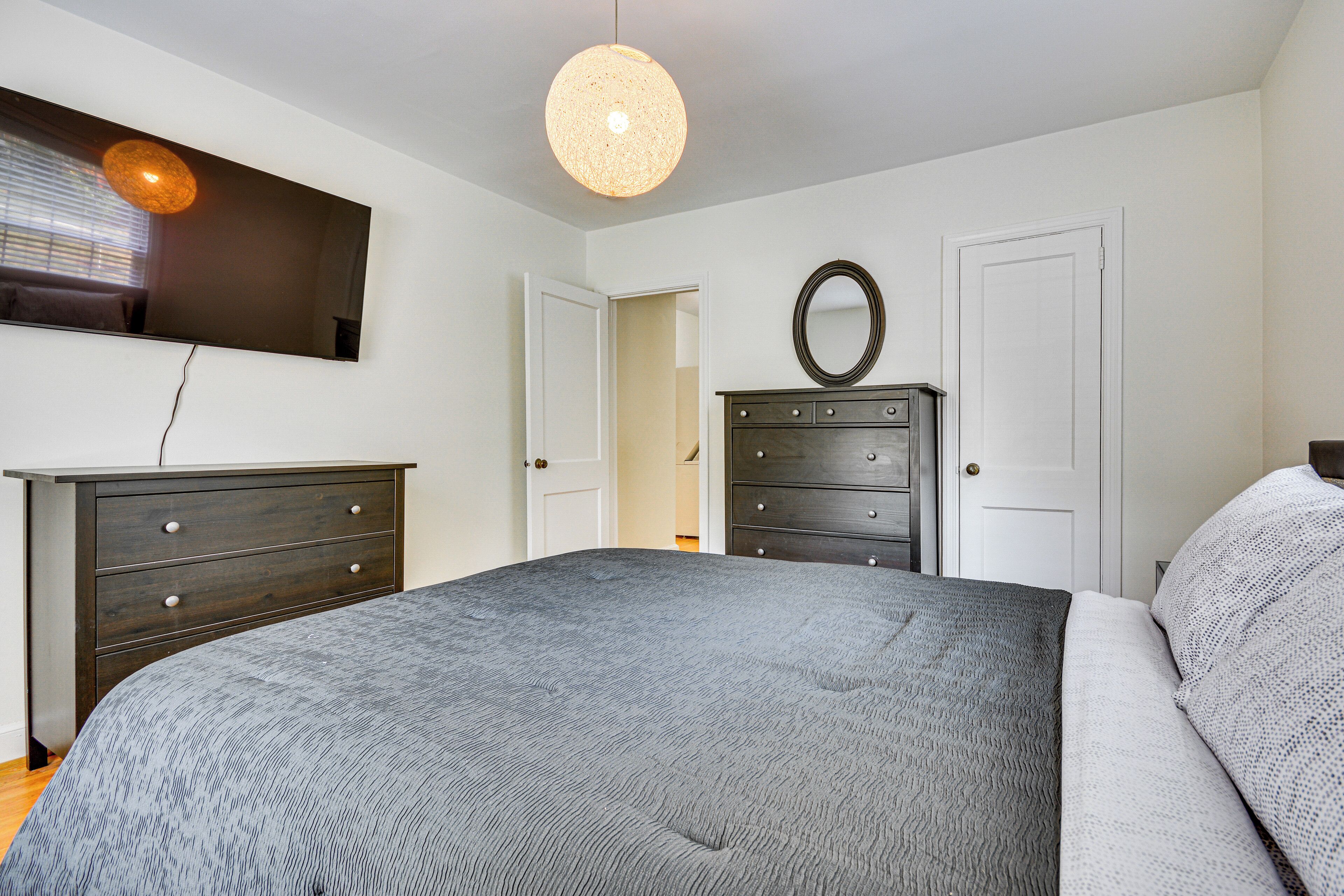 A bedroom with a bed, a dresser, a mirror, and a television on the wall.