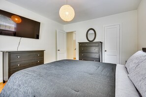 Une chambre à coucher avec un lit, une commode, un miroir et un téléviseur fixé au mur.