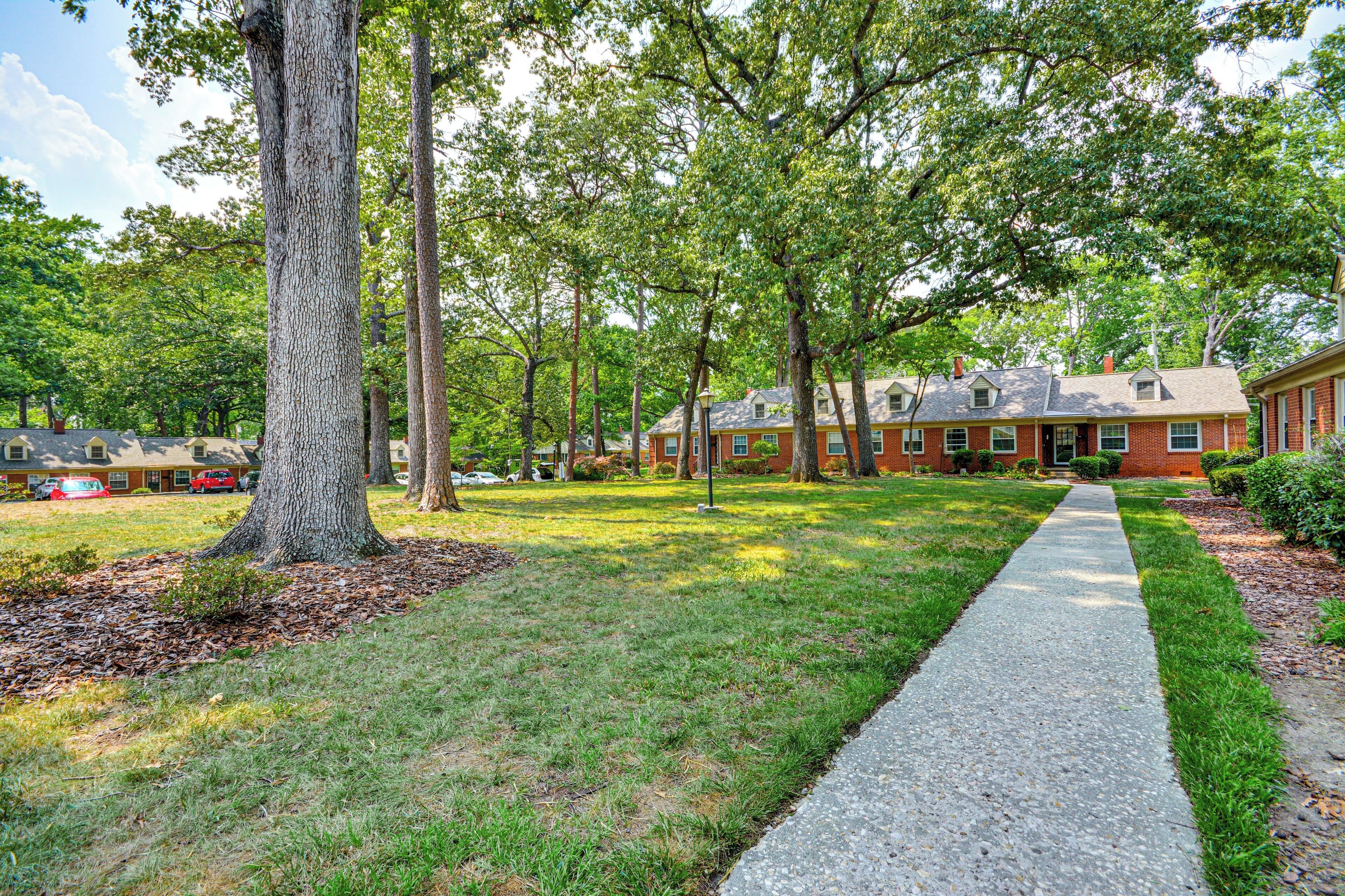 A residential area with a paved walkway, brick houses, and a large tree.