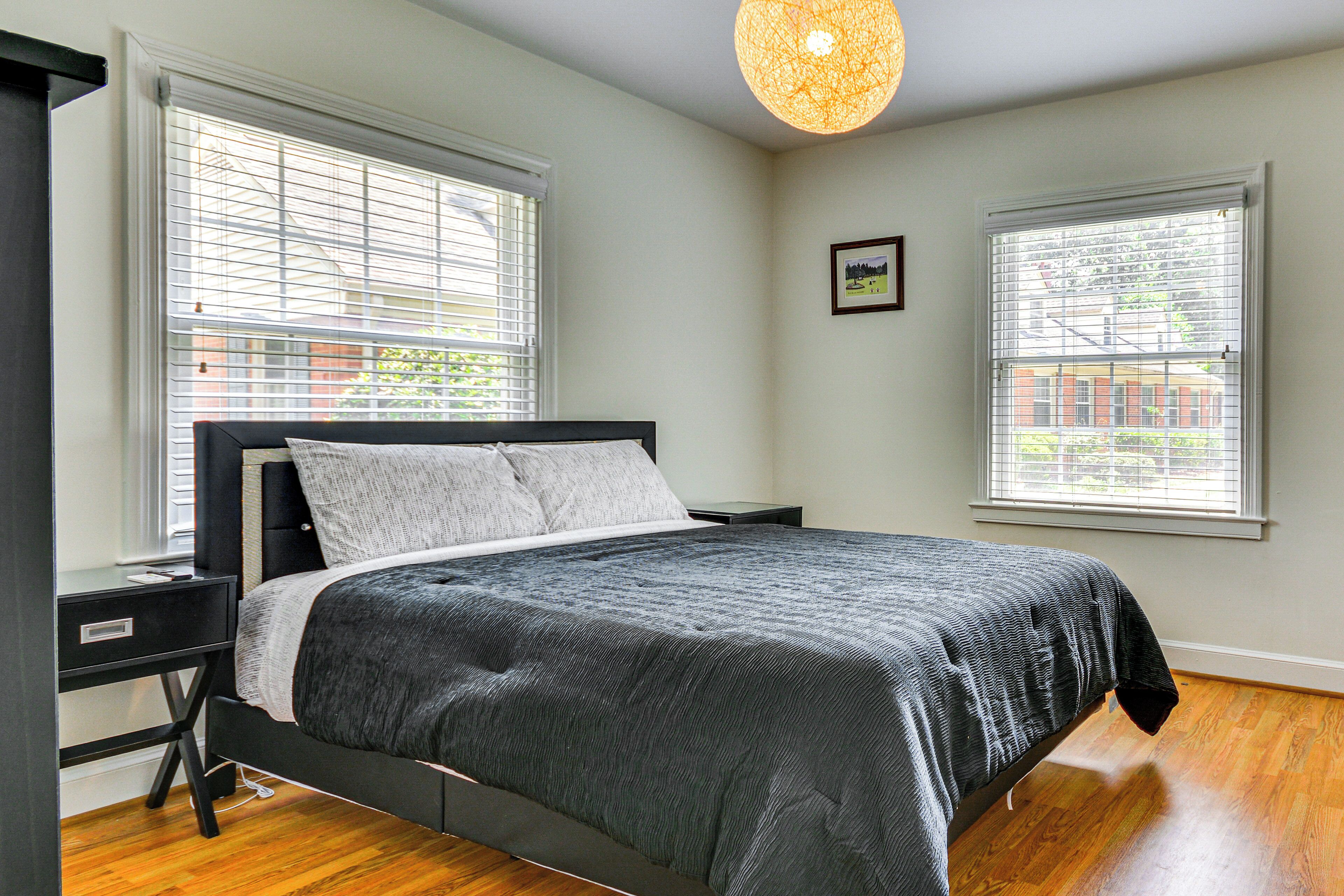A bedroom with a bed, a desk, and two windows with blinds.