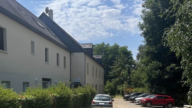 Una strada sterrata conduce a un edificio con diverse finestre e un'auto parcheggiata.
